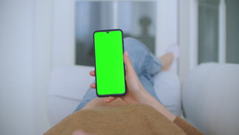 Close-up-shot-of-green-screen-template-smartphone-in-female-hands-at-home-girl-is-watching-content-without-touching-gadget-screen.-Modern-technology-and-information-concept.